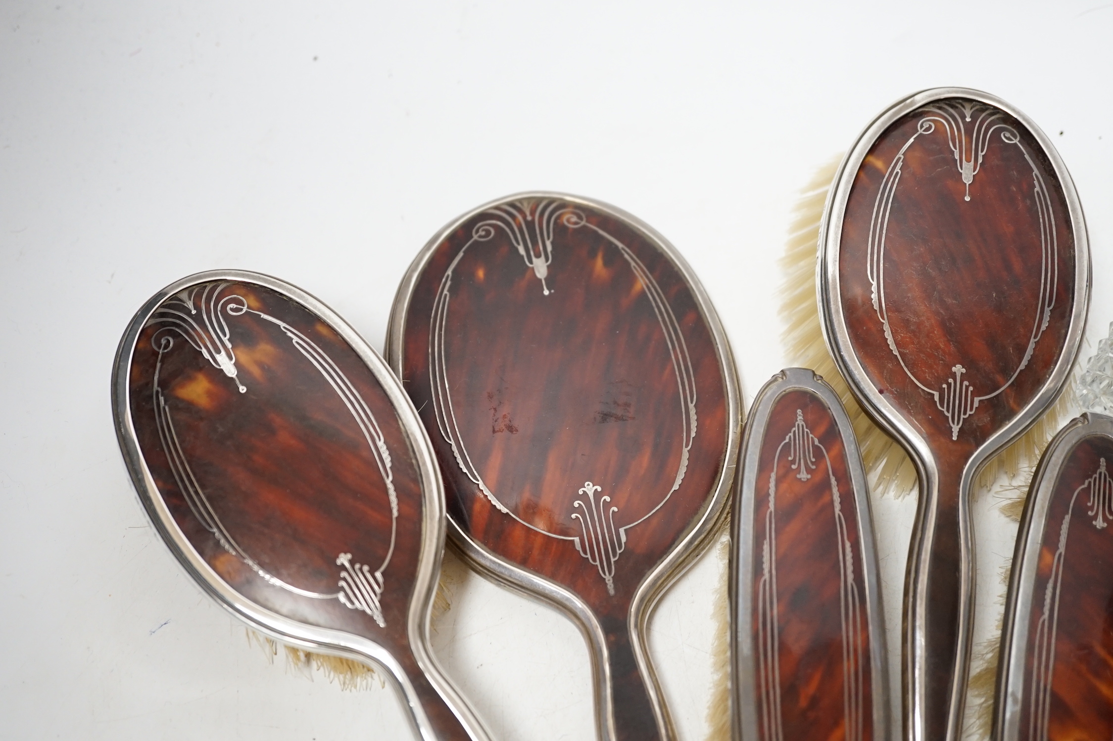 A George V silver and tortoiseshell pique mounted dressing table set, Adie Bros, Birmingham, 1934, and three silver topped toilet jars.
